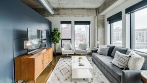 A modern living room with a large TV, two grey sofas, a white coffee table, and a large window with a city view. - Sable 508 - One Bedroom (Minneapolis)