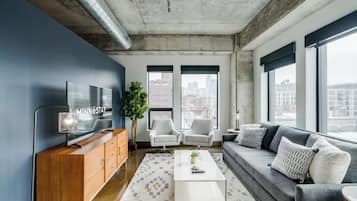 A modern living room with a large TV, two grey sofas, a white coffee table, and a large window with a city view.