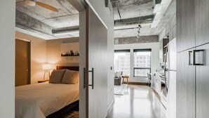 A modern hotel room with a bed, bedside table, and lamp. The room has a large window and a view of the city. - Sable 508 - One Bedroom (Minneapolis)