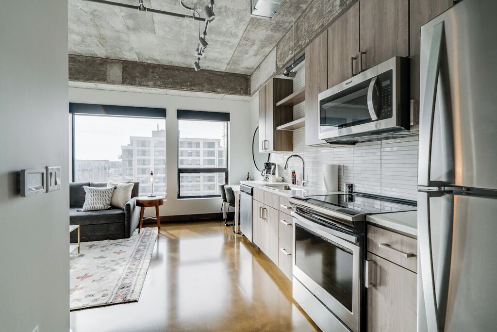 A modern kitchen with stainless steel appliances, wooden cabinets, and a large window providing a view of the city.