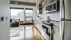 A modern kitchen with stainless steel appliances, wooden cabinets, and a large window providing a view of the city. - Sable 508 - One Bedroom (Minneapolis)