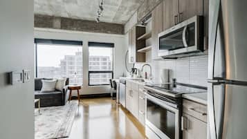 A modern kitchen with stainless steel appliances, wooden cabinets, and a large window providing a view of the city.
