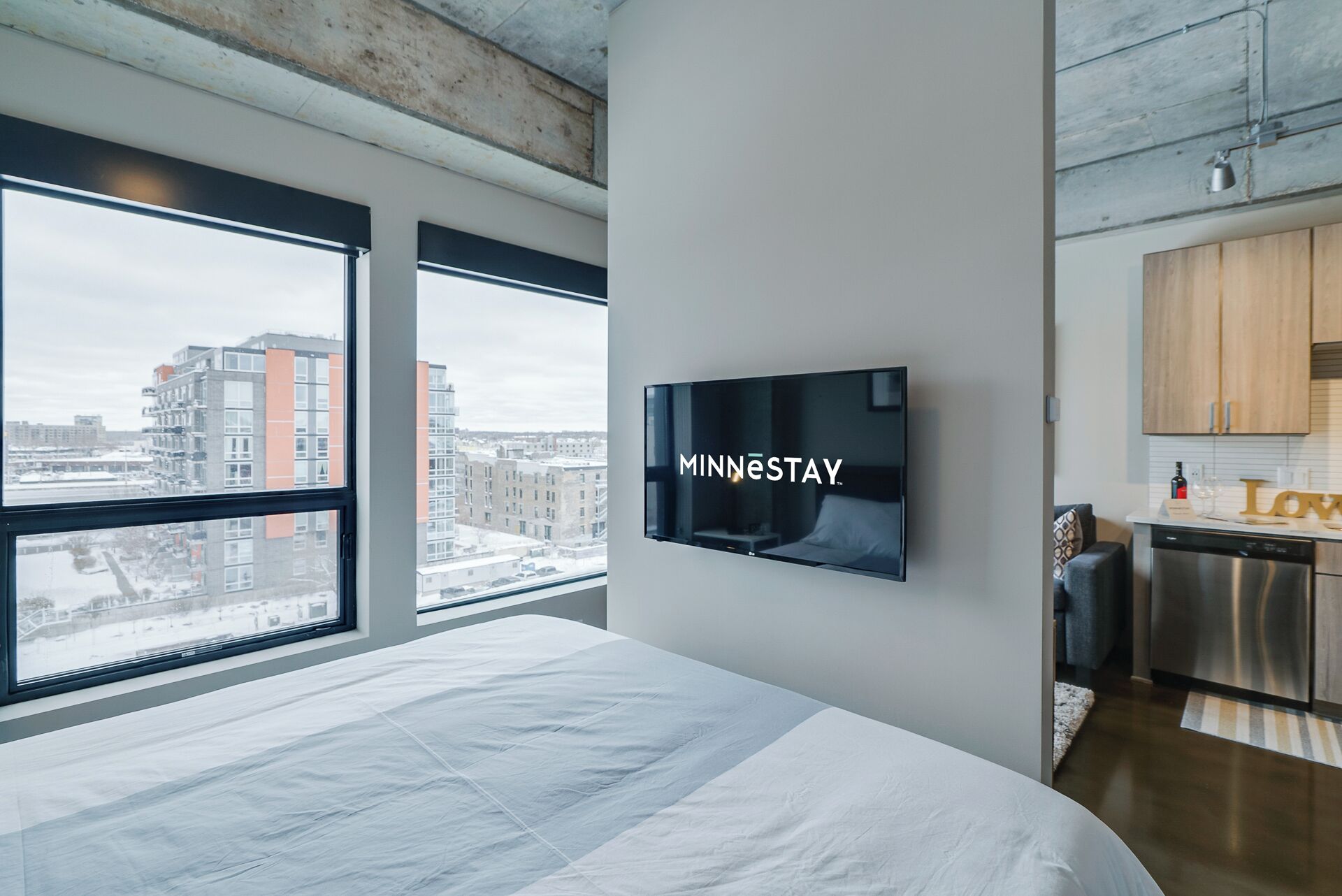 Ein modernes Hotelzimmer mit einem großen Bett, einem an der Wand befestigten Fernseher und Blick auf die Stadt durch große Fenster.