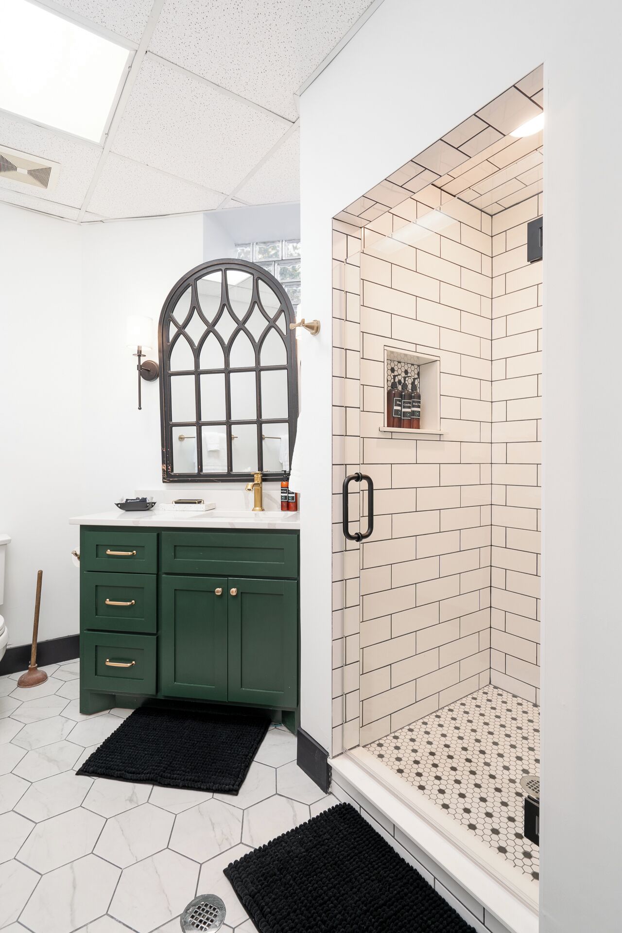 A modern bathroom with a green vanity, a large arched window, and a shower with hexagonal tiles.