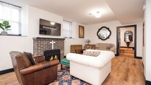 A living room with a fireplace, a sofa, a leather armchair, and a television mounted on the wall. - Lyndale Church Lodge (Minneapolis)