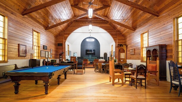 A spacious room with wooden walls and ceiling, a pool table, multiple seating areas, and a large arched window. - Lyndale Church Lodge (Minneapolis)