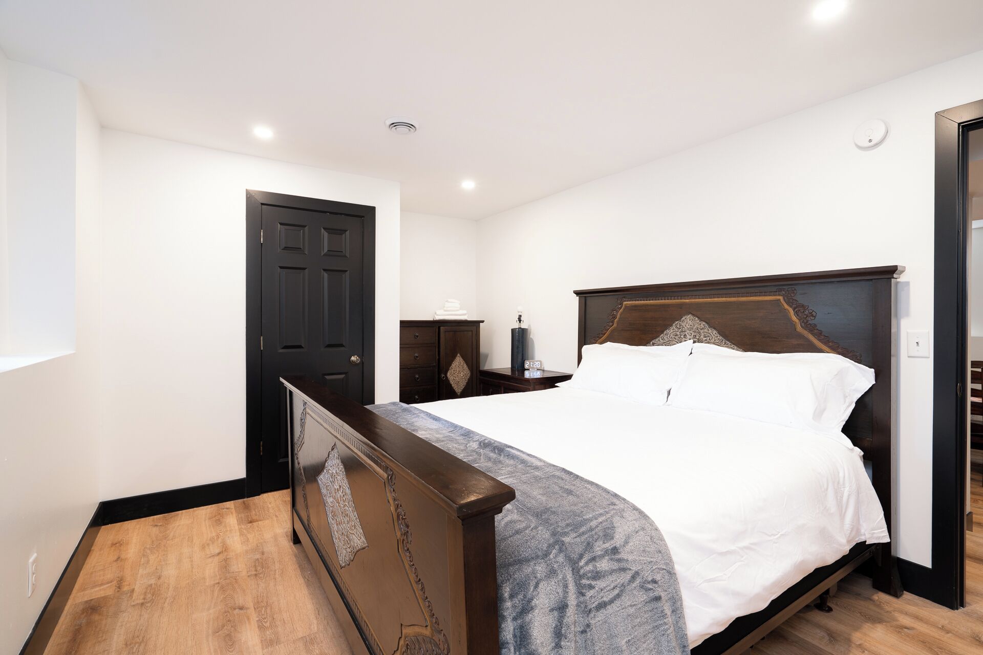 A bedroom with a wooden bed, a nightstand, a dresser, and a dark door.