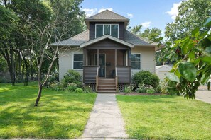A two-story house with a front porch, a small front yard, and a pathway leading to the entrance. - Cherokee Park Family Escape (St. Paul)