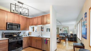 A modern kitchen with wooden cabinets, stainless steel appliances, and a dining area with a table and chairs. - Cherokee Park Family Escape (St. Paul)