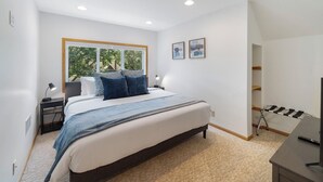 A modern bedroom with a large bed, bedside tables, a desk with a chair, and a window with a view of trees. - Cherokee Park Family Escape (St. Paul)