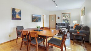 A modern living room with a dining area, featuring a wooden dining table, grey sofas, and a large window with a view of the outdoors. - Cherokee Park Family Escape (St. Paul)