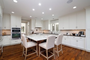 Una cocina moderna con armarios blancos, una isla central con sillas y electrodomésticos integrados.
