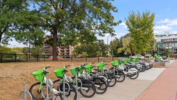 Een rij fietsen geparkeerd op een voetpad, elk met een groene mand en een bord dat aangeeft dat ze deel uitmaken van een fietsdeelsysteem.