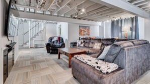 A spacious living room with a large sectional sofa, a wooden coffee table, and a TV mounted on the wall. A staircase with a white railing leads to an upper level. - Edina Escape (Minneapolis)