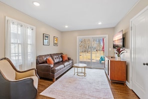 A living room with a brown leather sofa, a round coffee table, and a white door leading to a patio. - Haven in the Heights (Falcon Heights)