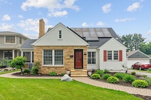 A two-story house with a stone facade, a red front door, and a solar panel roof. - Haven in the Heights (Falcon Heights)