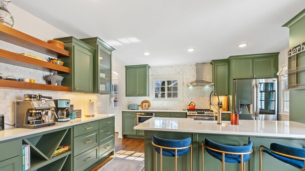 A modern kitchen with green cabinets, a central island with bar stools, a coffee machine, and a built-in oven. - Haven in the Heights (Falcon Heights)