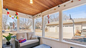 A covered porch with a wicker sofa, a small table, and a suitcase. - Haven in the Heights (Falcon Heights)