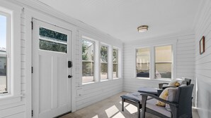 A sunroom with white walls, large windows, a wicker chair, and a small table.