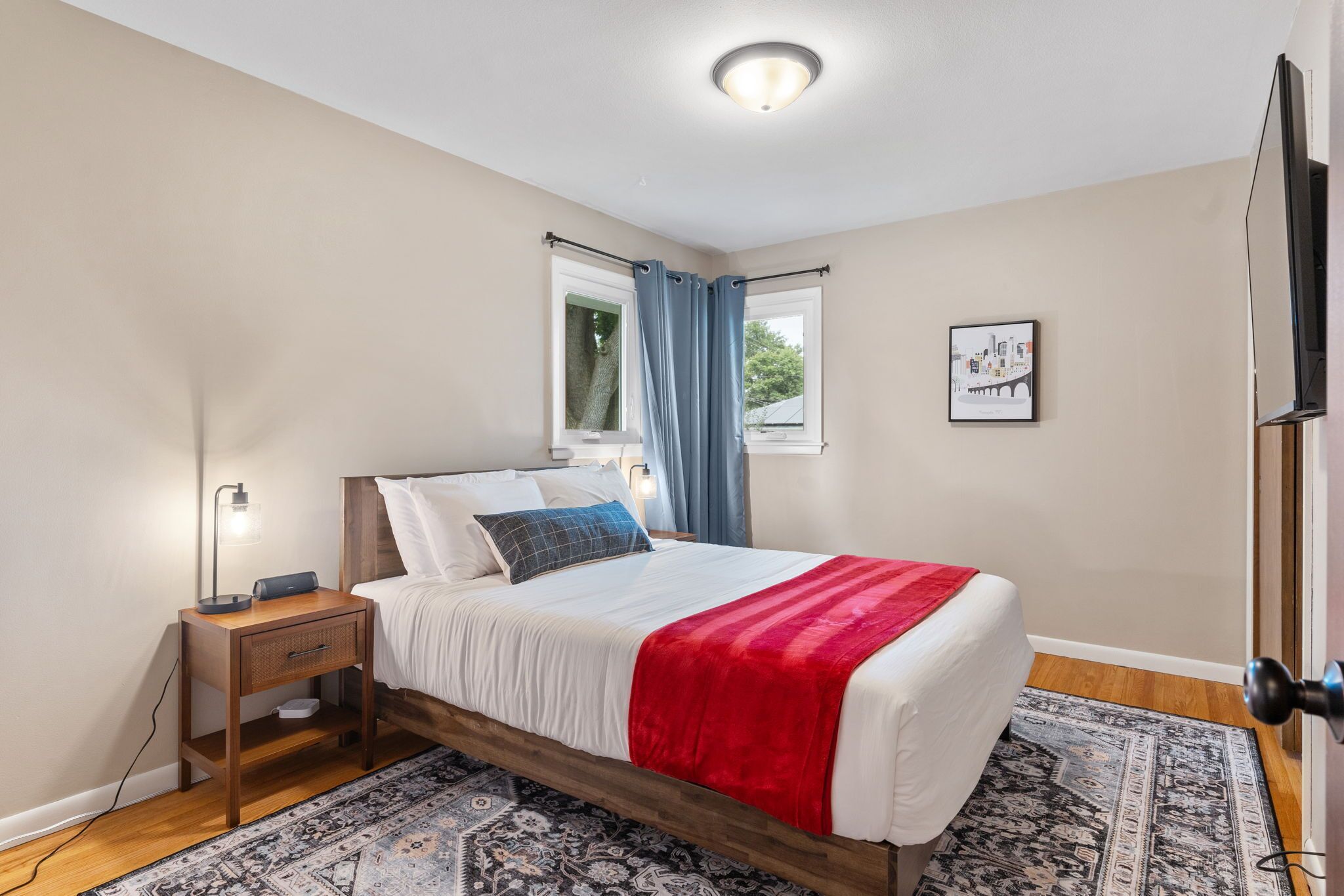 Una camera da letto ordinata con un letto, un comodino, una lampada e una finestra con tende.
