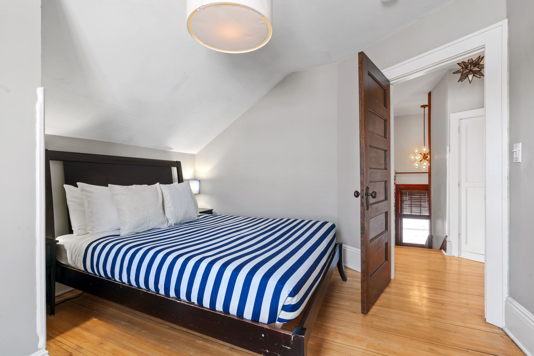 Een slaapkamer met een bed, een houten vloer, witte muren en een plafondlamp.