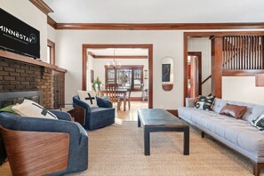 A living room with a fireplace, two sofas, a coffee table, and a dining area with a chandelier. - Fulton Lodge (Minneapolis)