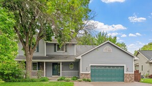 A two-story house with a front porch, a garage, and a well-maintained lawn. - Ultimate Family Fun Escape (Champlin)