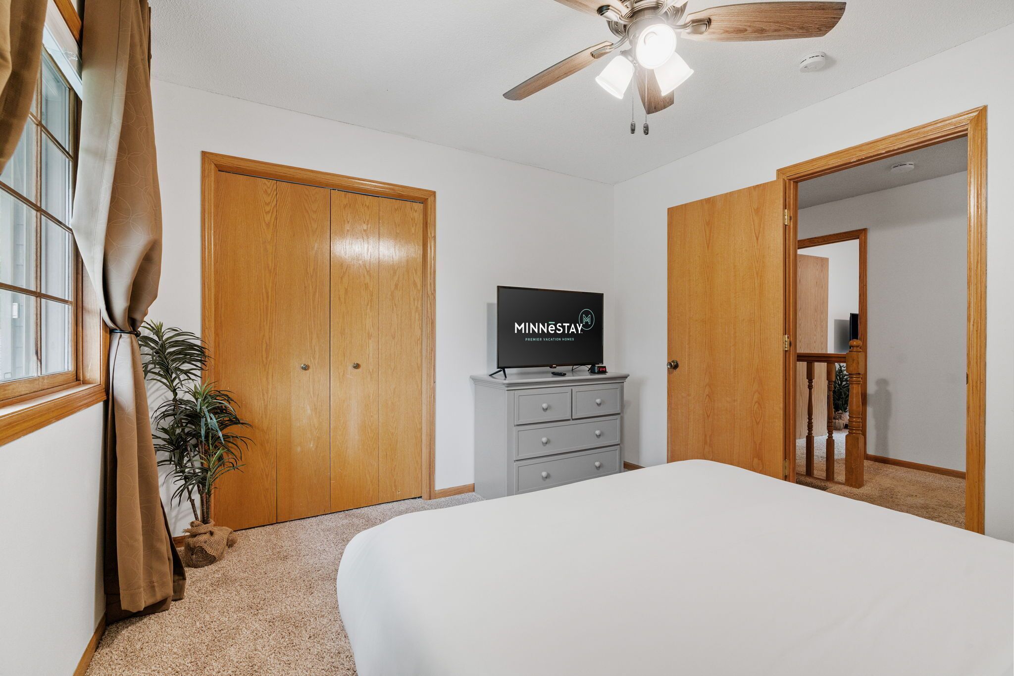 Una camera da letto con un letto, una ventola a soffitto, una TV su una cassettiera e porte in legno.