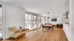 A spacious living area with a large window, a dining table, and a TV mounted on the wall. - Modern Chic (Lake Elmo)