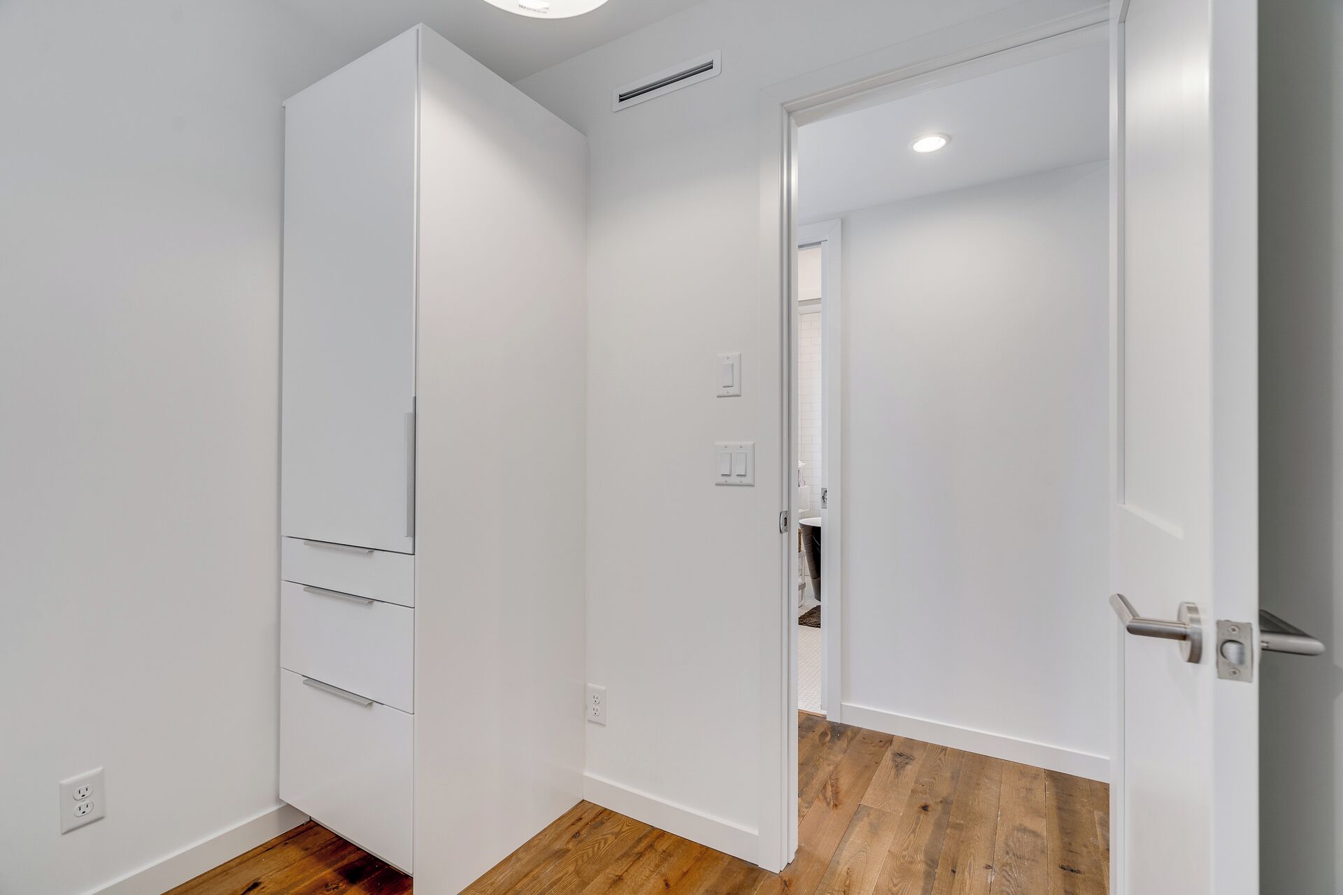 Ein Flur mit einem weißen Kleiderschrank, einer Tür zu einem Badezimmer und einem Holzboden.