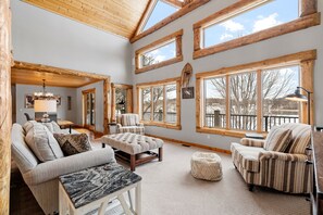 A spacious living room with high ceilings, large windows, and a cozy fireplace. - Maple Lake Chalet (Buffalo)