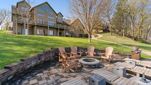 Μια βεράντα με ξαπλώστρες Adirondack, μια εστία για φωτιά και έναν τοίχο από πέτρα.