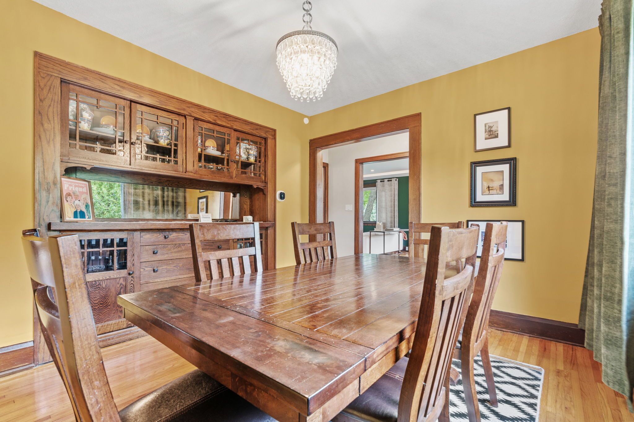 Comedor con mesa y sillas de madera, una araña y armarios de madera con vajilla.