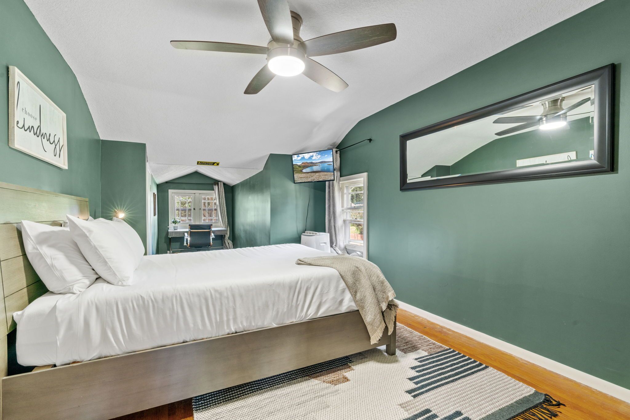 A bedroom with a bed, a ceiling fan, a TV, and a window.