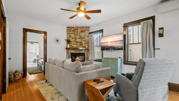 A living room with a fireplace, a sofa, a chair, a wooden coffee table, and a ceiling fan. - Lyndale Pleasant Getaway (Minneapolis)