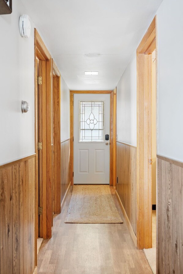 A hallway with wooden paneling, a white door with a glass panel, and a textured rug on the floor. - Lake Pulaski Getaway (Buffalo)
