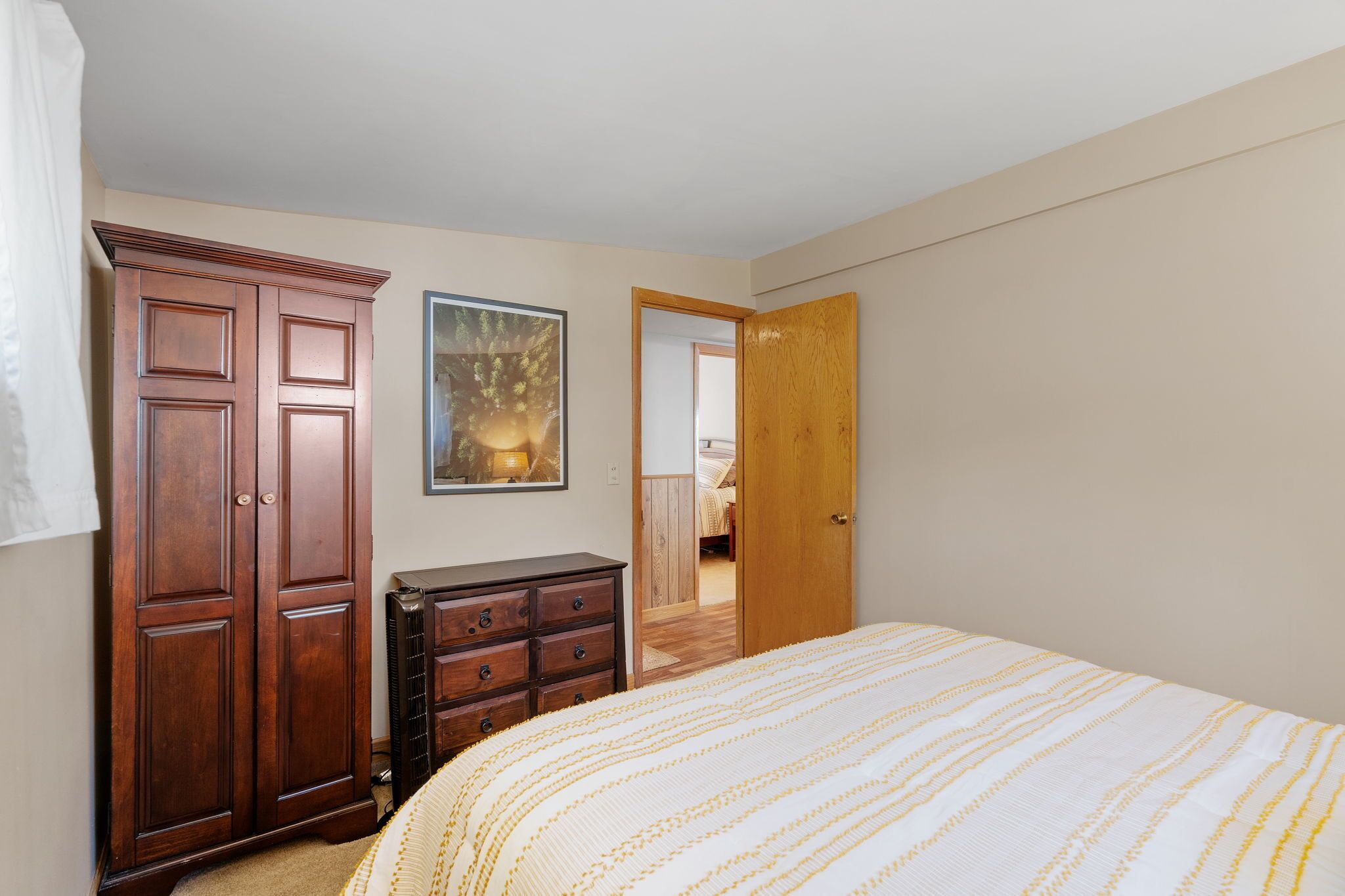 A bedroom with a bed, a wardrobe, a dresser, and a door leading to another room.