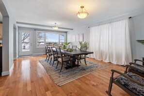 Un coin repas avec une table en bois, des chaises et un tapis. Deux lampes suspendues sont placées au-dessus de la table.