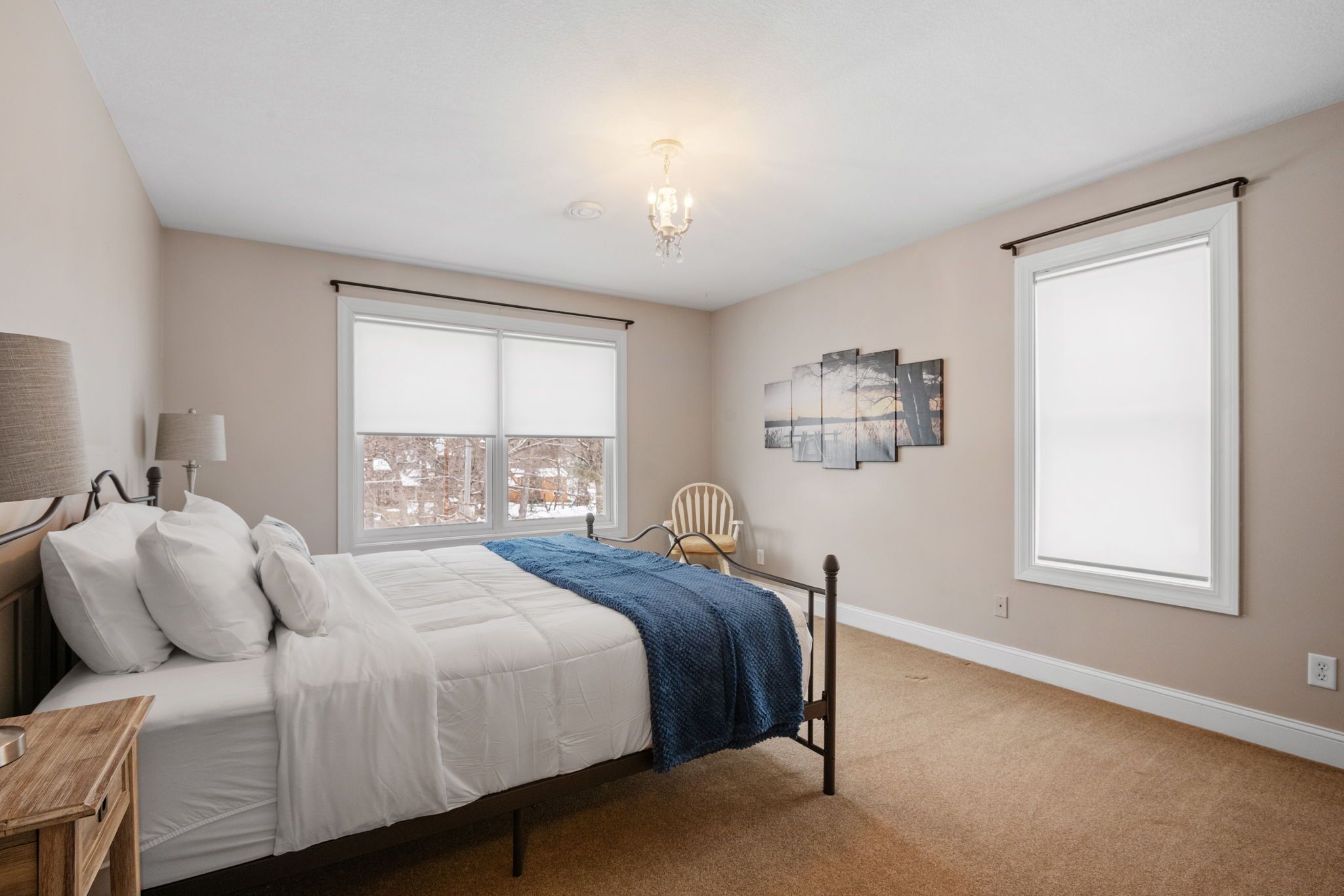 A bedroom with a bed, a chair, a lamp, and artwork on the wall.