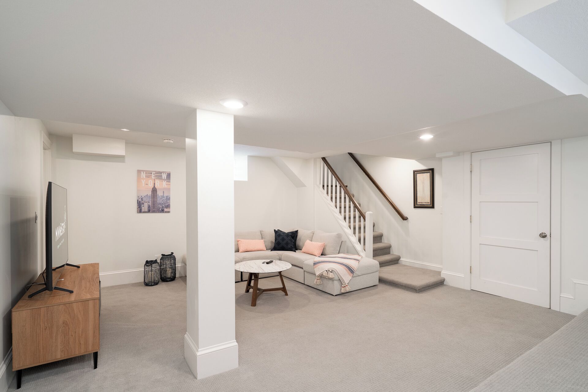 A spacious living room with a sofa, a coffee table, and a TV stand. There is a staircase leading to another level.