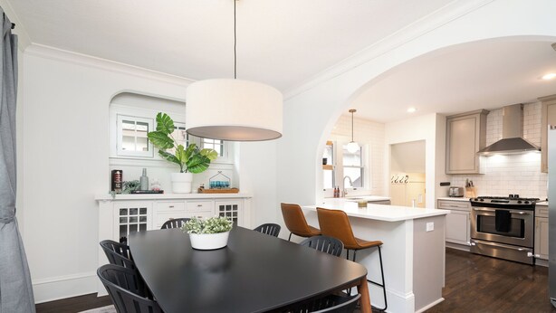 A modern kitchen with white cabinetry, a central island, and a dining area with a black table and chairs. - Fulton Gates (Minneapolis)