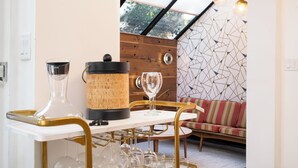 Zona pranzo con tavolo bianco, sedie dorate e parete in legno. Sulla tavola si vedono bicchieri da vino e una bottiglia di vino con tappo.