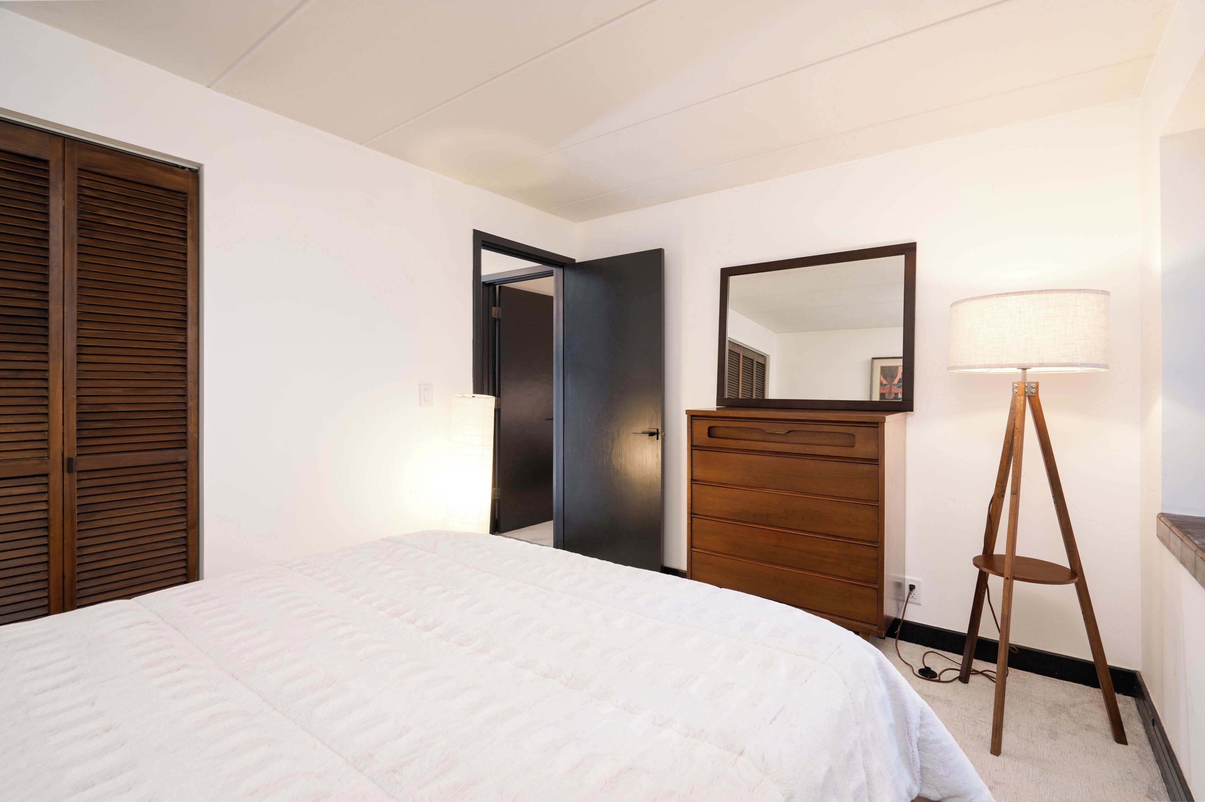 A bedroom with a bed, a dresser, a mirror, and a lamp.