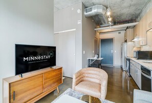 A modern living room with a flat-screen TV, wooden entertainment unit, and a plush armchair. - Sable 302 - Alcove (Minneapolis)