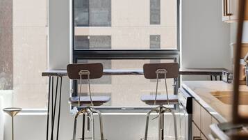 A modern kitchen with two bar stools, a window with blinds, and a view of a building outside.