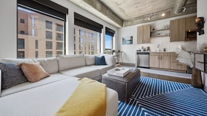 A modern hotel room with a sofa, ottoman, and a view of the cityscape.