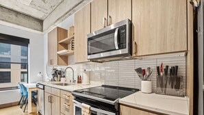 A modern kitchen with wooden cabinets, a stainless steel microwave, a black stove, and a countertop with kitchen utensils. - Sable 204 - One Bedroom (Minneapolis)