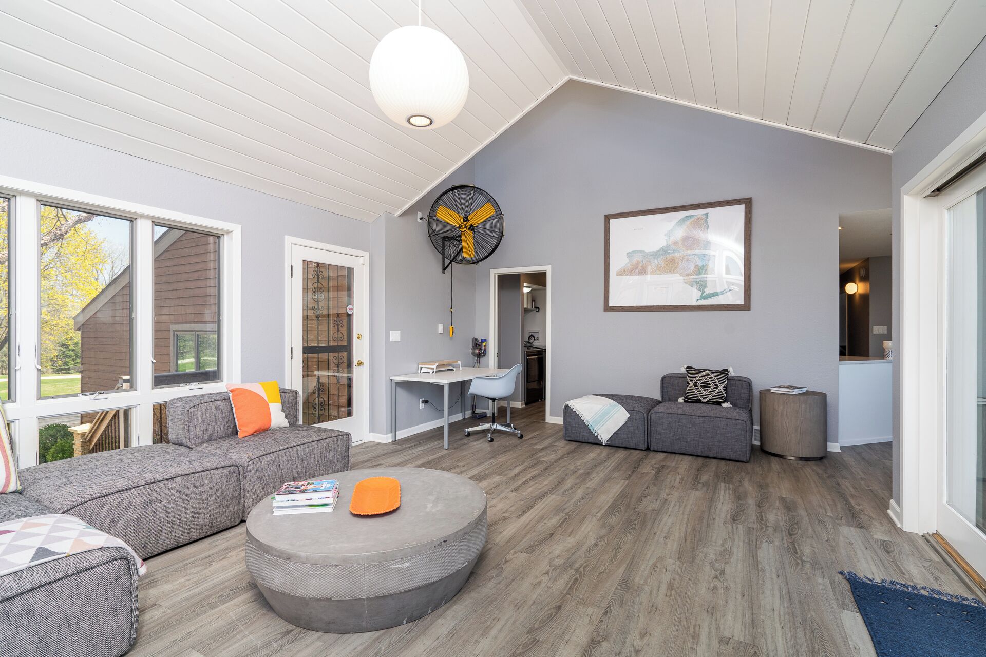 A spacious living room with a large gray sofa, a round ottoman, and a dining area with a table and chairs.