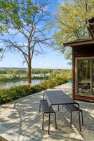 Una terraza de madera con dos bancos de metal, con vista a un lago y un paisaje boscoso.