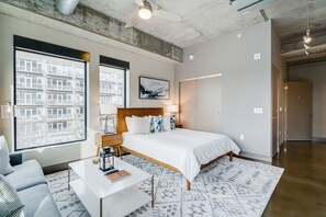 A modern hotel room with a large bed, a desk, and a view of the city through large windows. - Sable 301 - Studio (Minneapolis)